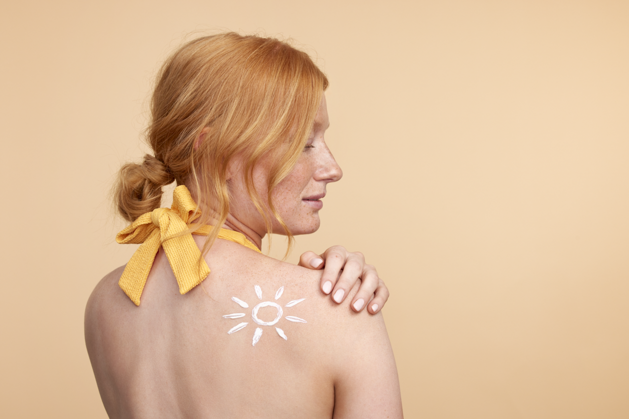 Roodharige vrouw met zonnebrand crème op der schouder in de vorm van een zon